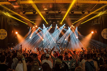 Energetic music concert scene with bright lights and a lively cheering crowd indoors. HD wallpaper