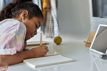 A young girl concentrating on homework at home using a tablet. HD wallpaper