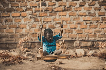 A young boy enjoys a playful moment swinging outdoors in front of a rustic brick wall. HD wallpaper