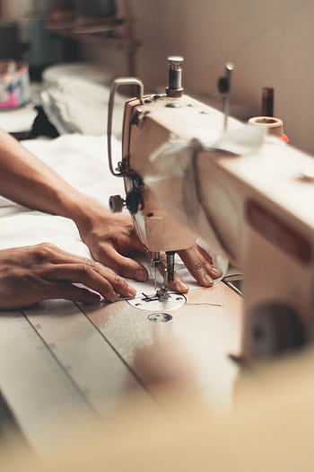 Close-up of hands using a sewing machine, depicting craftsmanship and textiles indoors. HD phone wallpaper