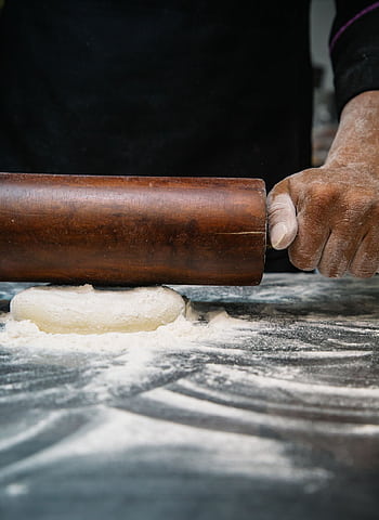 Close-up of a chef rolling dough with a wooden pin, capturing the art of baking. HD phone wallpaper