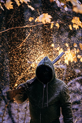 A mysterious figure in a hooded sweater carries a rifle in a snowy forest with backlit snowfall. HD phone wallpaper