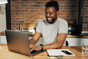 African American man smiling while working remotely on laptop from home office HD wallpaper