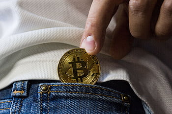 Close-up of hand putting Bitcoin in jeans pocket symbolizing cryptocurrency savings. HD wallpaper