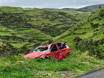 A red wrecked car lies abandoned in a scenic green valley, highlighting rural decay. HD wallpaper