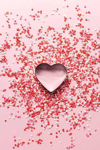 Festive heart-shaped cookie cutter surrounded by pink and red confetti for Valentine's Day. HD phone wallpaper
