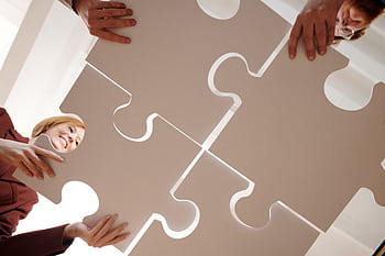 Low angle view of diverse team assembling large puzzle pieces, symbolizing unity and cooperation. HD wallpaper