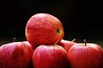 A cluster of ripe, red apples stacked on a dark backdrop highlighting their freshness and vibrancy. HD wallpaper