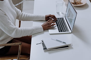 A person typing on a laptop in a minimalistic home office setting, capturing modern work culture. HD wallpaper