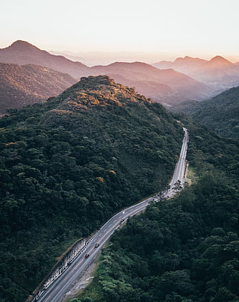 Drone captures a winding road through lush mountains at sunrise, offering stunning scenery. HD phone wallpaper