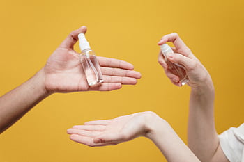 Hands using hand sanitizer against a yellow background, highlighting hygiene. HD wallpaper