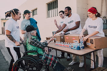 Volunteers distribute bottled water and supplies to diverse individuals in an outdoor setting, showcasing community support. HD wallpaper