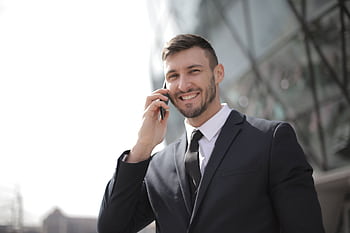 Smiling businessman in a suit having a call outside a modern glass building. HD wallpaper