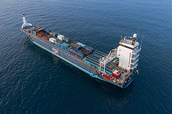 A drone captures a vibrant container ship navigating deep blue ocean waters. HD wallpaper