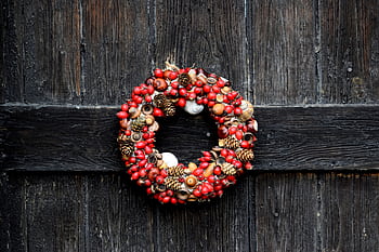 A festive red and brown wreath with natural elements on a rustic wooden door. HD wallpaper