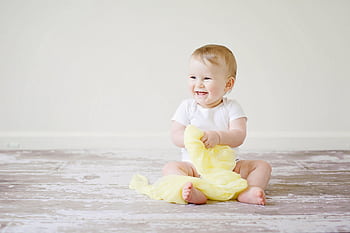 Adorable baby laughing while sitting on the floor with a yellow blanket indoors, showcasing happiness and innocence. HD wallpaper
