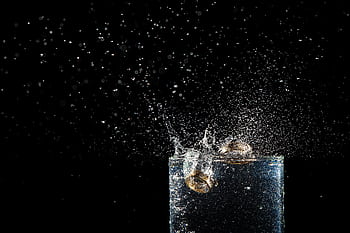 Close-up of wedding rings creating water splash in a glass with black background. HD wallpaper