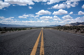 A straight road stretches into the desert horizon under a cloud-filled blue sky. HD wallpaper