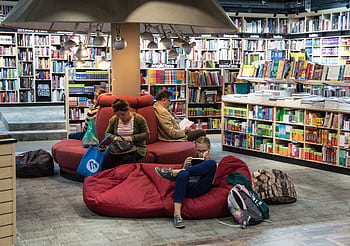 A welcoming library space with people relaxing and reading on comfortable seating. HD wallpaper