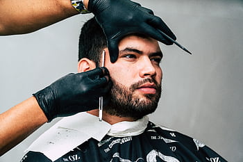 Man receiving a precise beard trim in a barbershop, showcasing expert grooming skills. HD wallpaper