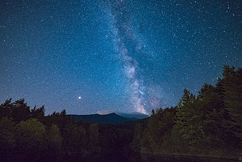 A breathtaking view of the Milky Way galaxy shining brightly over a serene forest landscape at night. HD wallpaper