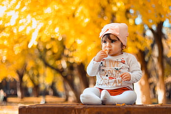 A cute baby girl sitting on a bench enjoying a sunny fall day in a park. HD wallpaper