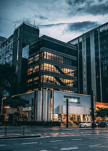 Night view of a city block with illuminated store, modern architecture, and cloudy sky. HD phone wallpaper