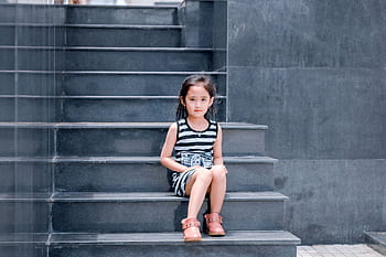 A young girl in a striped dress sits on a sleek grey staircase, looking into the camera. HD wallpaper