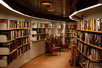 A cozy library space in Stockholm with brown leather chairs and wooden bookshelves filled with books. HD wallpaper