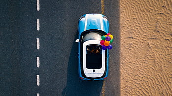 A Mini Cooper with colorful balloons drives along a desert road. Captured from above. HD wallpaper