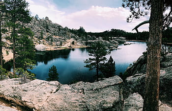 Serene lake surrounded by rocky hills and conifer trees in Custer State Park, South Dakota. HD wallpaper