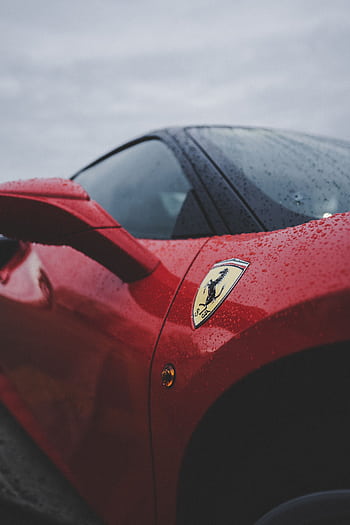 Detailed close-up of a red luxury sports car featuring rain droplets and emblem, evoking speed and elegance. HD phone wallpaper