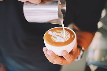 Close-up of a barista pouring latte art into a coffee cup indoors. HD wallpaper