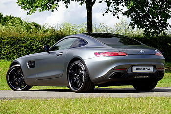 A luxury Mercedes AMG GT in silver, parked outdoors by trees on a sunny day. HD wallpaper