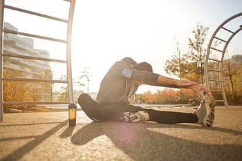 A man stretches in a park wearing activewear, focused on his fitness routine at sunrise. HD wallpaper