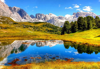 Breathtaking view of mountains reflected in a serene lake, surrounded by lush greenery and clear blue skies. HD wallpaper