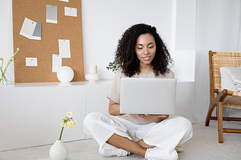 Young woman with curly hair working on her laptop in a cozy home setting, exuding confidence and focus. HD wallpaper