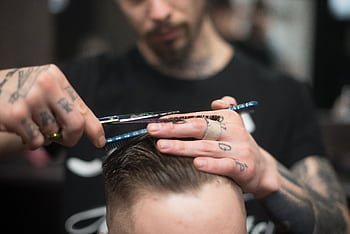 A tattooed barber provides a precise haircut in a modern barbershop setting. HD wallpaper