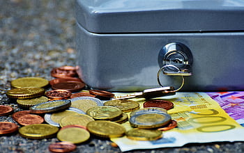 Close-up of a secure cash box with euro coins and banknotes, symbolizing wealth and financial security. HD wallpaper