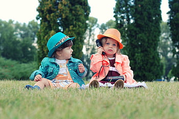 Two toddlers in colorful outfits enjoying playtime with walkie talkies in a sunny park setting. HD wallpaper