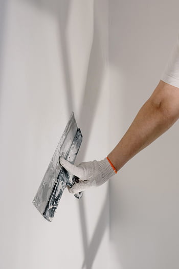 Hand in glove plastering a wall with a trowel indoors, enhancing smoothness. HD phone wallpaper