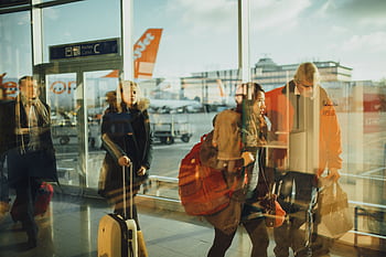 Passengers moving through an airport gate area with visible airplanes outside. HD wallpaper