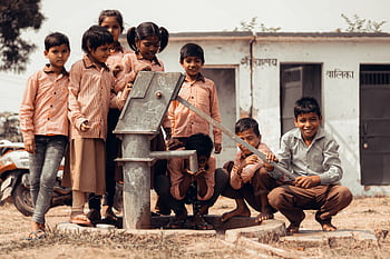 A group of Indian children gather joyfully around a manual water pump outdoors. HD wallpaper