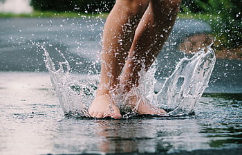 Bare feet splashing in a puddle, capturing the joy of a rainy day outdoors. HD wallpaper
