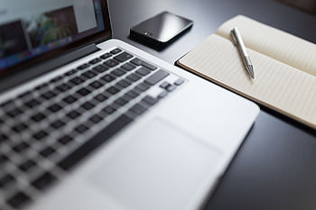 A modern workspace featuring a laptop, notebook, smart, and pen on a desk. HD wallpaper