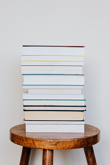 A neat stack of books placed on a rustic wooden stool, perfect for reading scenes. HD phone wallpaper