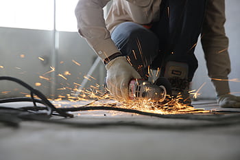 A skilled industrial worker uses a grinder creating a burst of sparks indoors. HD wallpaper