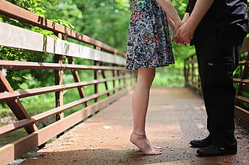 A barefoot couple holding hands on a wooden bridge in a lush green setting, symbolizing romance. HD wallpaper