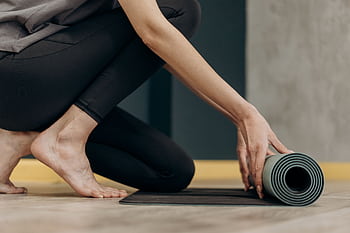 A woman rolling out a yoga mat for an indoor fitness routine, emphasizing calmness and focus. HD wallpaper
