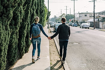 A couple walks hand in hand along a sunny sidewalk in an urban area, showcasing romance and companionship. HD wallpaper